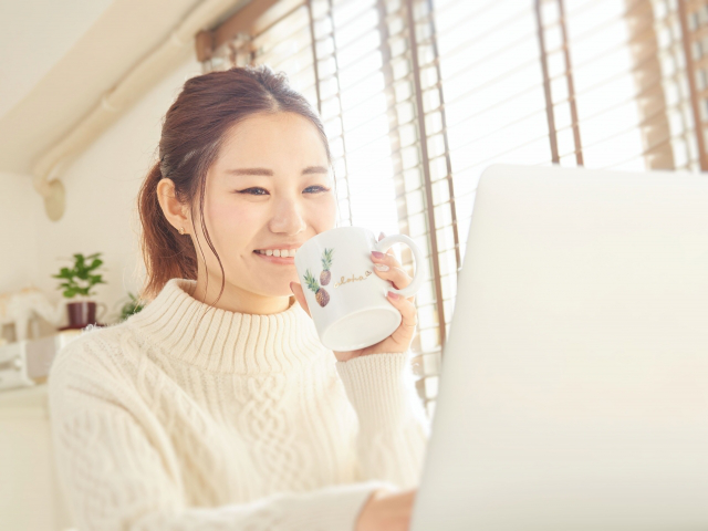ホットドリンクを飲みながらパソコン作業をする女性